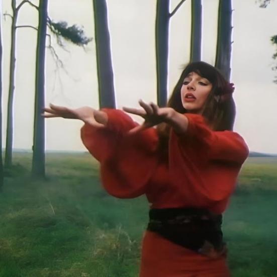 Kate Bush i rødklædt dans under åben himmel. 