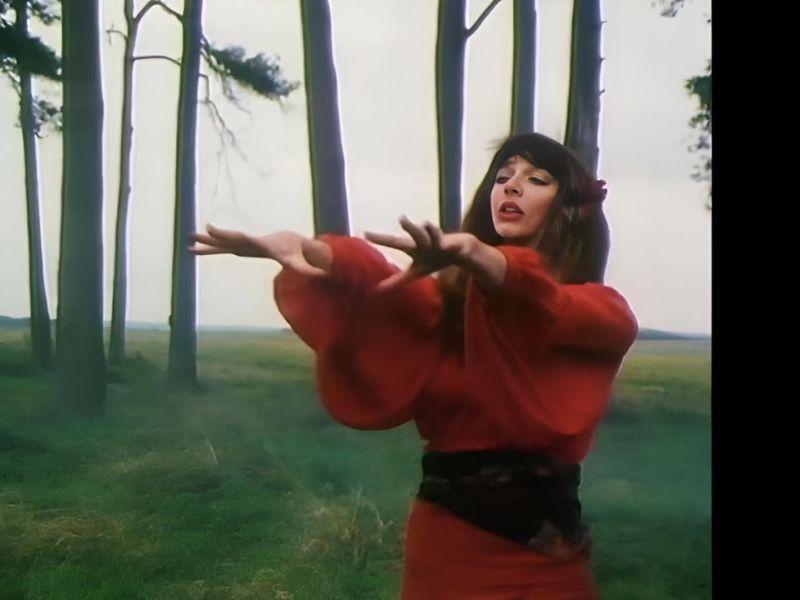 Kate Bush i rødklædt dans under åben himmel. 