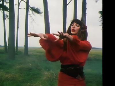 Kate Bush i rødklædt dans under åben himmel. 